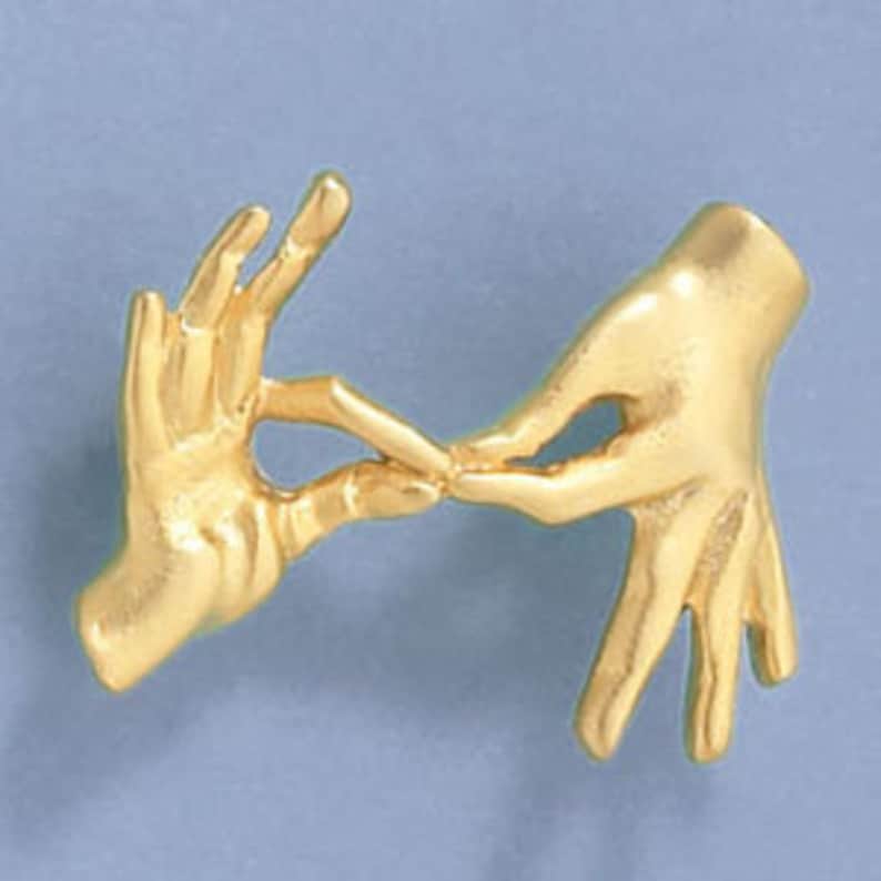 May include: Gold-toned metal brooch featuring two hands clasped together in a gesture of love or friendship.