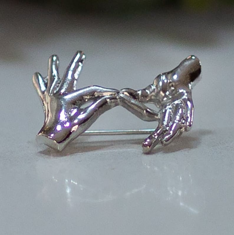 May include: Silver brooch featuring two hands clasped together in a gesture of friendship or love.