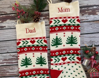 Puede incluir: Dos calcetines de Navidad de punto blanco con patrones rojos y verdes. Los calcetines están personalizados con los nombres "Mamá" y "Papá".