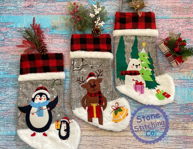 May include: Three grey and white Christmas stockings with red and black checked cuffs. The stockings feature embroidered designs of a penguin, a reindeer, and a polar bear. The stockings are decorated with faux fur and are ready to be filled with gifts.