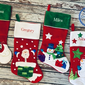 May include: Four red Christmas stockings with white cuffs and green tops, each embroidered with a name. Festive designs include a sleigh with gifts, Santa Claus, snowmen, and stars. The Stone Stitching Co. logo is in the top right corner.