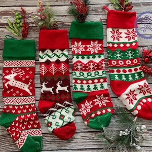 May include: Four red and green Christmas stockings with different patterns. The stockings are made of knitted fabric and have a traditional Christmas design.