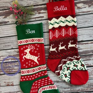May include: Two red and green knitted Christmas stockings with white embroidered names "Ben" and "Bella". The stockings feature a reindeer design and a traditional Scandinavian pattern.