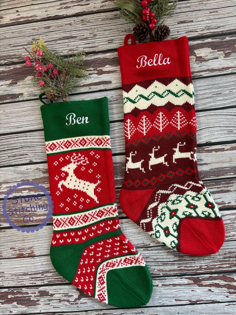 May include: Two red and green knitted Christmas stockings with white embroidered names "Ben" and "Bella". The stockings feature a reindeer design and a traditional Scandinavian pattern.