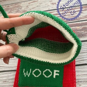 May include: Red and green knitted stocking with a white cuff and the word "WOOF" embroidered in white on a green background. The stocking is turned inside out to show the knit pattern.
