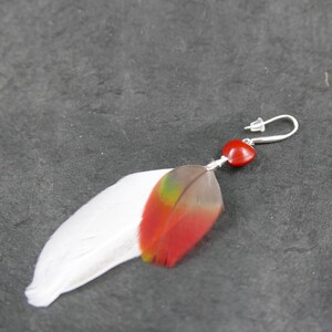 Puede incluir: Un pendiente de plumas rojo, verde y blanco con una cuenta roja en forma de corazón y un gancho plateado.