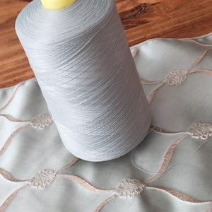May include: A spool of light blue thread with a yellow plastic top. The thread is wound tightly and is ready to be used for sewing or embroidery.