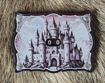 Può includere: Un gettone di gioco in pelle marrone con un'illustrazione di castello argentato e due dadi che mostrano il numero "0".