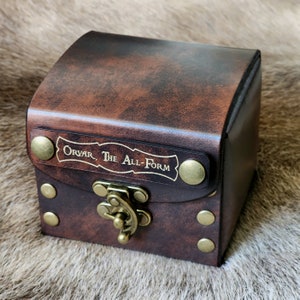 May include: A small, brown leather box with a brass clasp and metal studs. The box has a label that reads "Orvar, The All-Form".