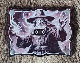 May include: A black and white illustration of a wizard with a long white beard and a pointed hat. The wizard is holding a glowing orb in his left hand and his right hand is raised in the air. The wizard is wearing a dark robe with a belt and a chain around his neck. The background is a dark gray with white lightning bolts. The image is on a wooden plaque with silver metal accents. The plaque has a small black counter with the numbers "00" on it.