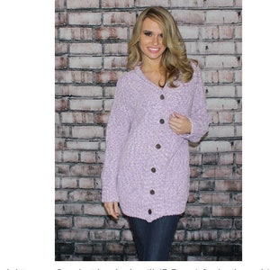 May include: A lavender knitted cardigan with a button closure. The cardigan is shown on a model and in close-up shots. The text "520 Cambridge Cardigan" is at the top of the image. The text "Materials: #4 Worsted weight yarn. Crochet hook size 'I' (5.5mm) for body and 'G' (4.0mm) for ribbing. Six-eight 1 ½' buttons. Size: Directions are for size Small. Changes for Medium, Large and Extra large are included. INTERMEDIATE" is at the bottom of the image.