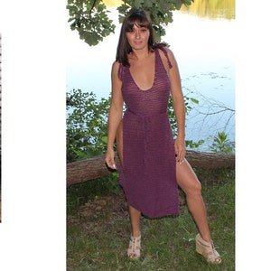 Puede incluir: Una túnica de ganchillo de color morado con un nudo en los hombros. La túnica tiene un escote en V profundo y una abertura a cada lado. La modelo lleva la túnica con un par de sandalias marrones. 808 Shoulder Tied Tunic.