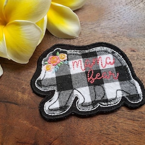 May include: Black and white checkered fabric bear applique with red embroidery that says "mama bear" and a small floral design on the head.