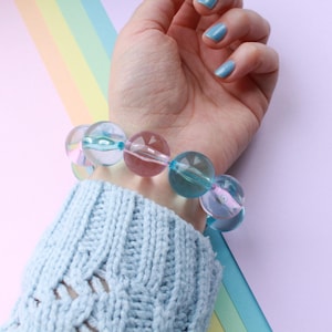 Könnte beinhalten: Ein Armband aus großen, runden, transparenten Perlen mit rosa und blauen Wirbeln. Die Perlen sind auf einer durchsichtigen Gummikordel aufgefädelt.