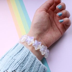 May include: A white iridescent star-shaped beaded bracelet on a person's wrist.