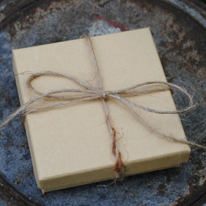 May include: A brown cardboard box wrapped with twine and tied with a bow. The box is sitting on a rustic metal surface.