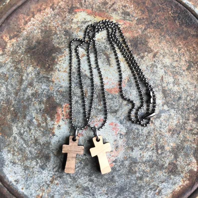 May include: Two wooden cross pendants on silver ball chains. The crosses are light brown and have a natural wood grain.