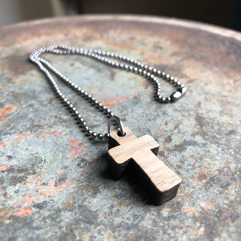 May include: A wooden cross pendant on a silver ball chain necklace. The cross is dark brown with a lighter wood grain visible.