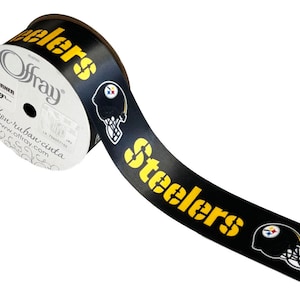 May include: Black and yellow ribbon with the word "Steelers" and a football helmet logo. The ribbon is rolled up on a white spool with the text "Offray" and "ribbon ruban cinta" printed on it.