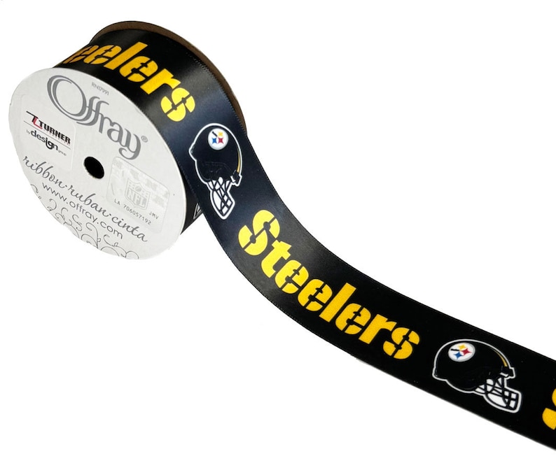 May include: Black and yellow ribbon with the word "Steelers" and a football helmet logo. The ribbon is rolled up on a white spool with the text "Offray" and "ribbon ruban cinta" printed on it.