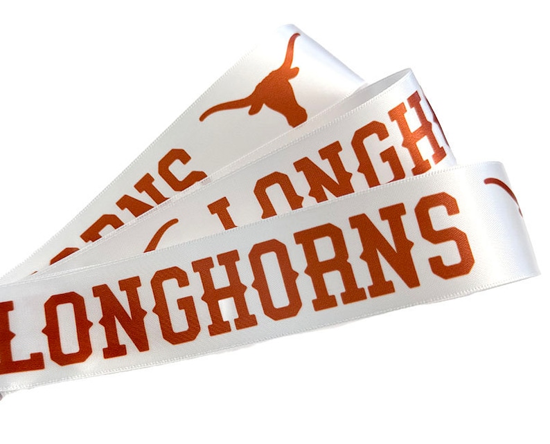 May include: White satin ribbon with the words "Longhorns" printed in orange. The ribbon also features a stylized orange Longhorn steer head.