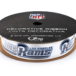 Könnte beinhalten: Eine Rolle weißes Band mit einem blauen und grauen Los Angeles Rams Logo, das sich auf dem Band wiederholt. Das Band befindet sich auf einer schwarzen Spule mit dem aufgedruckten Text "DECORATIVE RIBBON CINTA DECORATIVA 2012 NFL PROPERTIES, LLC Offray www.offray.com".