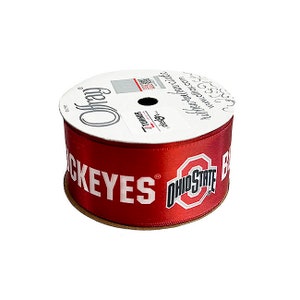 May include: A spool of red satin ribbon featuring the words "BUCKEYES" and "OHIO STATE" in white. The ribbon is from Offray and has a white label with text and a QR code.