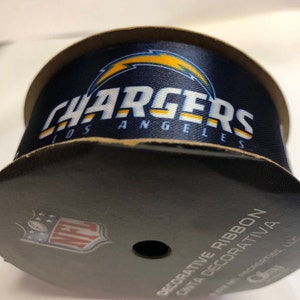 May include: A roll of blue and yellow decorative ribbon with the Los Angeles Chargers logo and the NFL logo. The ribbon is labeled "Decorative Ribbon Cinta Decorativa".