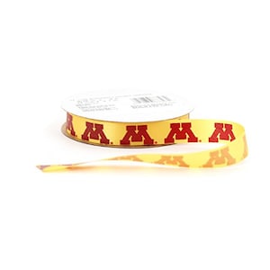 Pode incluir: Um rolo de fita amarela com logotipos "M" vermelhos impressos nele. A fita está sobre um fundo branco.