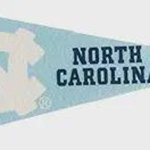 Puede incluir: Bandera triangular azul claro con las palabras "NORTH CAROLINA" en texto azul oscuro. La bandera presenta un gran logotipo blanco entrelazado "NC". Una franja vertical azul oscuro está en el lado izquierdo.