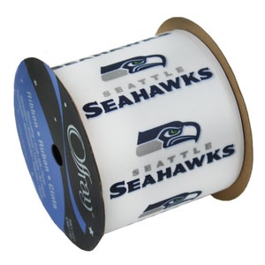 Peut inclure: Bobine de ruban blanche avec le logo et le nom des Seahawks de Seattle en bleu marine et gris. Le ruban présente un motif répété du logo de l'équipe, une tête de faucon stylisée et le nom de l'équipe. Fabriqué par Offray.