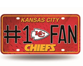 May include: Red metal license plate with the text "Kansas City #1 Fan Chiefs" in black and yellow lettering. The plate features a red, white, and yellow logo of the Kansas City Chiefs.