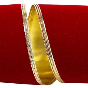 May include: A wide roll of deep red velvet ribbon featuring a smooth, matte texture on the front and a metallic gold finish on the reverse side. The edges of the ribbon are reinforced with a thin, shimmering gold wire trim for structure.