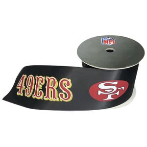 May include: A roll of black ribbon featuring the text "49ERS" in gold with a red outline, and the team logo in red and white. The ribbon also has the NFL logo on the spool.
