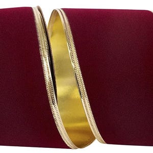 May include: A wide, deep burgundy velvet ribbon featuring a smooth, matte texture on the front and a reflective, metallic gold finish on the reverse side. The edges of the ribbon are finished with a thin, raised gold metallic trim.