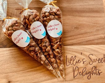 May include: Three clear plastic cones filled with chocolate-covered almonds. The cones are on a wooden surface and have a label that says "Lillie's Sweet Delights".