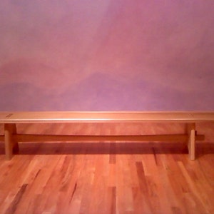 May include: A light wood bench with a simple design. The bench has a flat top and two legs on each end. The bench is sitting on a wooden floor.