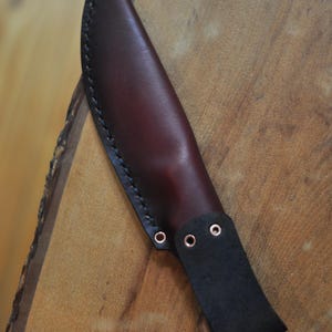 Pode incluir: Uma bainha de faca de couro bord&ocirc; feita &agrave; m&atilde;o. A bainha apresenta uma presilha de cinto de couro preto com tr&ecirc;s ilh&oacute;s e &eacute; costurada com linha preta. O design &eacute; simples e funcional, adequado para uso ao ar livre ou utilit&aacute;rio.