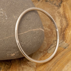 May include: A simple silver bangle bracelet, shown on a textured stone background.