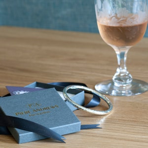 Op de afbeelding: Een zilveren armband in een grijze doos met een zwart lint. De doos heeft de tekst "P.A. Pierre Andrews Fine Jewellery" op de bovenkant.