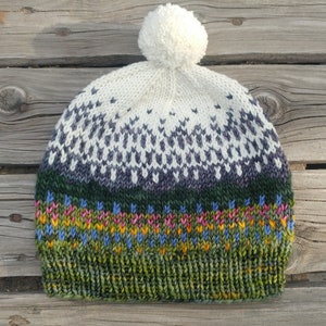 May include: A white knit hat with a pom pom on top. The hat has a green, pink, and blue patterned band around the bottom.