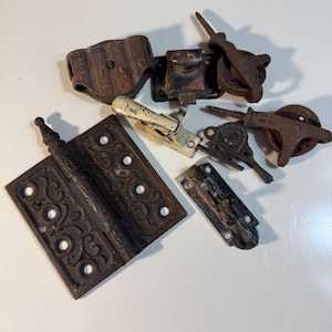 May include: A collection of antique metal hardware pieces, including hinges, latches, and pulleys. The items are primarily dark brown with signs of rust and wear, suggesting age and use. The hinge has an ornate design.