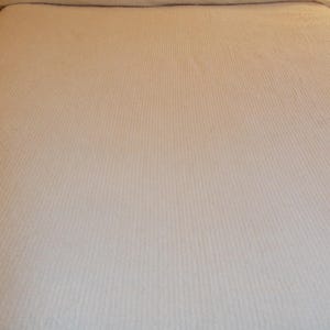 May include: A pale bedspread with a ribbed texture on a bed. The headboard has a black and white geometric pattern. The bedspread looks soft and inviting, suitable for a bedroom setting.