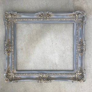 Puede incluir: Un marco de imagen de color gris y dorado con un dise&ntilde;o decorativo. El marco est&aacute; hecho de madera y tiene un acabado desgastado.