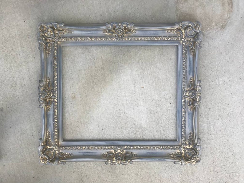 Puede incluir: Un marco de imagen de color gris y dorado con un dise&ntilde;o decorativo. El marco est&aacute; hecho de madera y tiene un acabado desgastado.