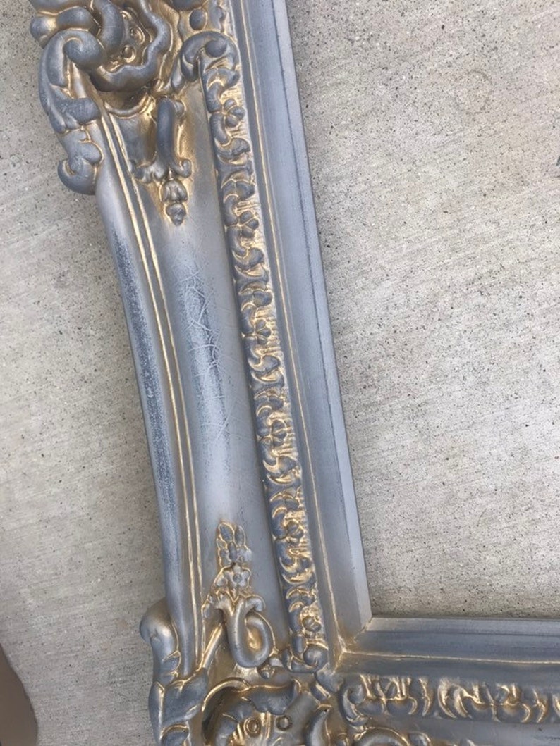 Puede incluir: Un marco de imagen adornado en plata y oro con un dise&ntilde;o detallado e intrincado. El marco est&aacute; hecho de madera y tiene un acabado desgastado.