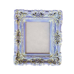 May include: A silver ornate picture frame with a light purple and gold finish. The frame has a decorative design with floral accents.