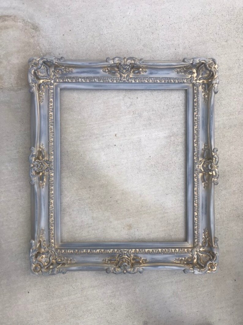 Puede incluir: Un marco de imagen adornado en gris y dorado con un dise&ntilde;o decorativo. El marco est&aacute; hecho de madera y tiene un acabado desgastado.