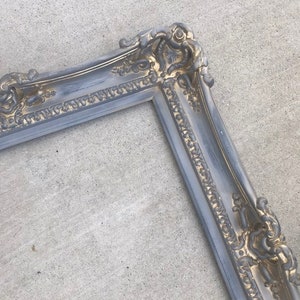 Puede incluir: Un marco de fotos ornamentado en plata y oro con un dise&ntilde;o detallado. El marco est&aacute; hecho de madera y tiene un acabado desgastado.