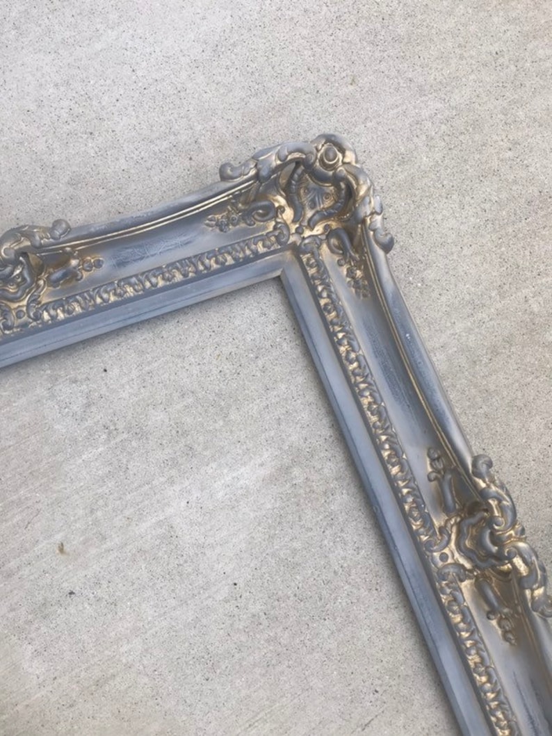 Puede incluir: Un marco de fotos ornamentado en plata y oro con un dise&ntilde;o detallado. El marco est&aacute; hecho de madera y tiene un acabado desgastado.